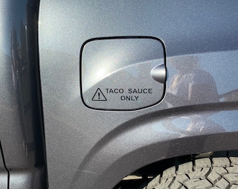 May include: A gray pickup truck with a gas cap that has a sticker on it that says "Taco Sauce Only" with an exclamation point.