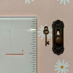 May include: A small, antique-style key and a decorative door knob with a round handle. Both are made of metal and have a bronze finish.