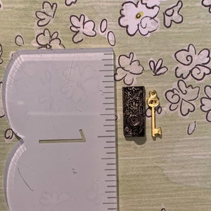 May include: A small, black metal keyhole cover with intricate details and a matching gold-toned key.