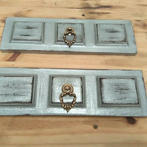 Pode incluir: Duas prateleiras de parede de madeira rústica com acabamento em pintura azul claro desgastada. Cada prateleira tem três compartimentos quadrados e uma maçaneta decorativa de latão.