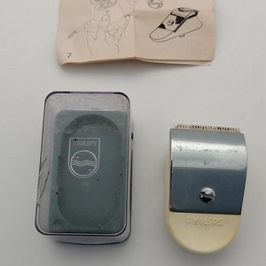 Può includere: Un tagliacapelli elettrico Philips SC 7917 con un corpo in plastica bianca e una lama in metallo argentato. Il tagliacapelli è mostrato accanto a una custodia in plastica trasparente con il logo Philips e un interno grigio.