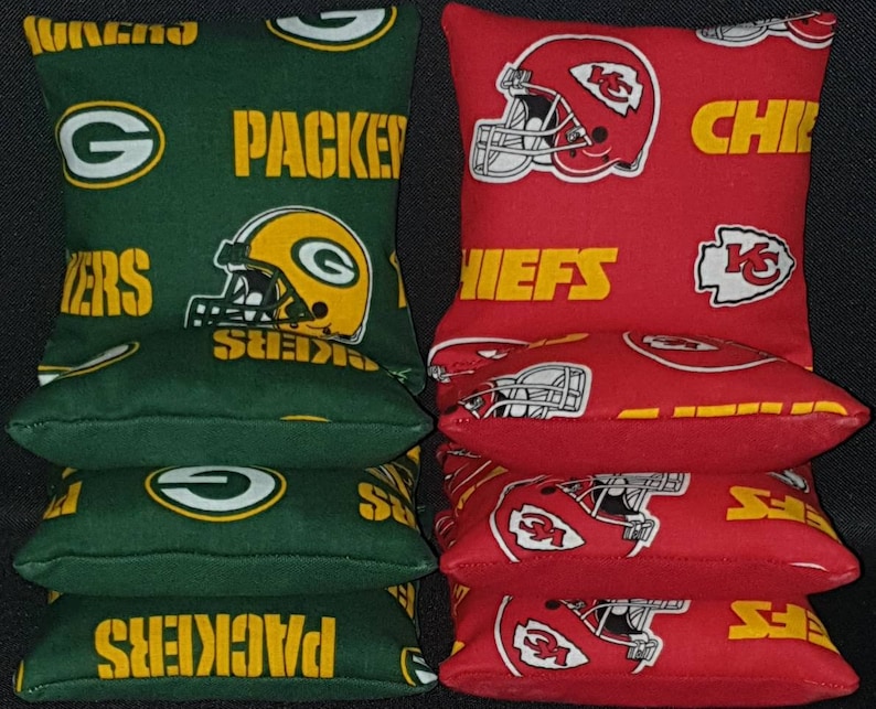 Pode incluir: Quatro sacos de feij&atilde;o verdes com o logotipo dos Green Bay Packers e a palavra "Packers" impressa neles. Quatro sacos de feij&atilde;o vermelhos com o logotipo dos Kansas City Chiefs e a palavra "Chiefs" impressa neles.