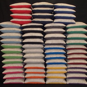 May include: A stack of 25 bean bags in various colors, including red, blue, green, yellow, orange, and purple. Each bean bag is made of a light gray fabric with a contrasting colored trim.