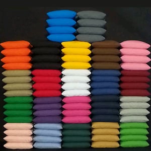 May include: A collection of colorful cornhole bean bags in various colors, including blue, orange, black, yellow, white, pink, and green. The bean bags are stacked in rows, showcasing a variety of options for outdoor games and activities.