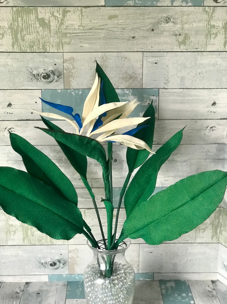 Breath taking and beautiful this Bird of Paradise felt flower is arranged in a vase with a 7 leaf bundle. 3 small leaves, 2 medium leaves, and 2 large leaves. The flower has 3 full blooms with off white tepals and medium blue petals. Gorgeous flower!