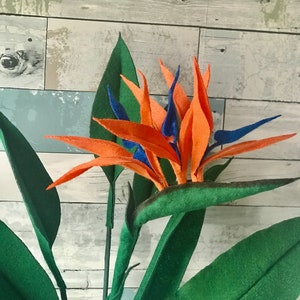Bird of Paradise felt flowers with orange tepals and blue petals surrounded by 7 leaves. 3 small leaves, 2 medium leaves, and 2 large leaves.