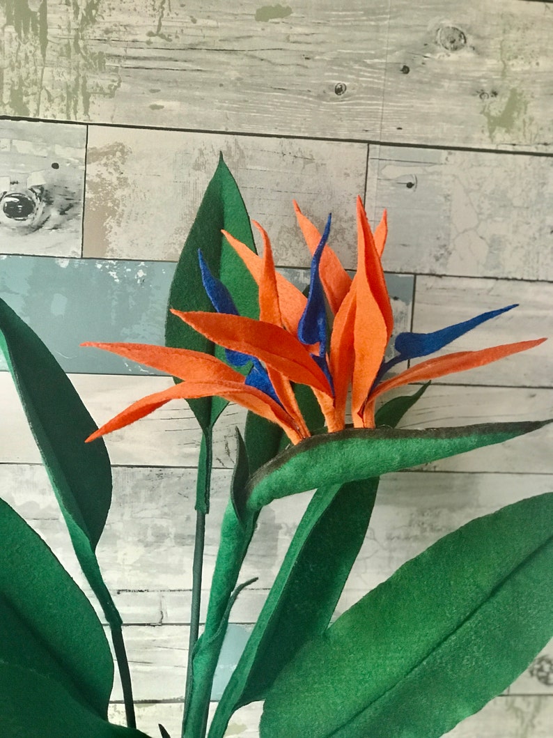 Bird of Paradise felt flowers with orange tepals and blue petals surrounded by 7 leaves. 3 small leaves, 2 medium leaves, and 2 large leaves.