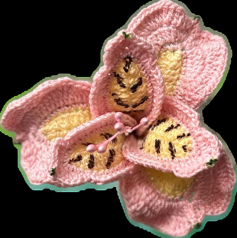 May include: A pink crocheted flower with yellow and brown accents. The flower has five petals and a center with a yellow and brown pattern.