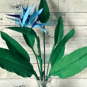 Bring the tropics to your home with this Bird of Paradise felt flower arrangement. 7 leaf bundle with 3 small leaves, 2 medium leaves, and 2 large leaves. The flower has 3 full blooms with of light blue tepals and dark blue petals. Spectacular flower