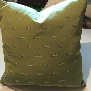 May include: A green cushion with a repeating pattern of small white and blue birds. The cushion is made of a soft, textured fabric.