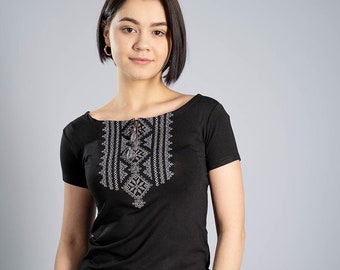 May include: A woman wearing a black short-sleeved shirt with a white embroidered design and blue jeans.