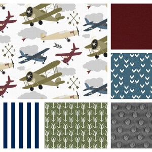May include: A collection of fabric swatches featuring various patterns, including a white background with airplanes, a solid burgundy fabric, a blue fabric with white chevron patterns, a navy blue and white striped fabric, a green fabric with white arrow patterns, and a gray fabric with a textured, bumpy surface.