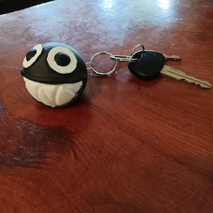 May include: A black and white character keychain with large eyes and a wide mouth. The keychain is attached to a silver key ring and a black key.