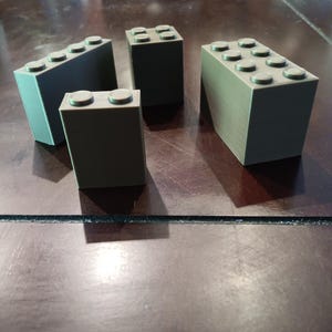 May include: Four green plastic toy building blocks of different sizes. The blocks are arranged on a dark brown wooden surface.