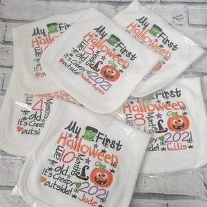 May include: A stack of white baby bibs with embroidered text that says "My First Halloween" and includes a pumpkin, witch hat, and stars. The bibs are personalized with different names and ages.
