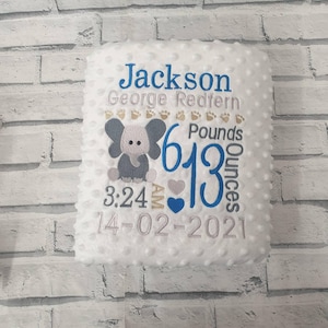 May include: White baby blanket with an embroidered elephant design. The blanket features the name "Jackson George Redfern", weight, time, and date. The blanket is 2.77 kg and 380 grams.