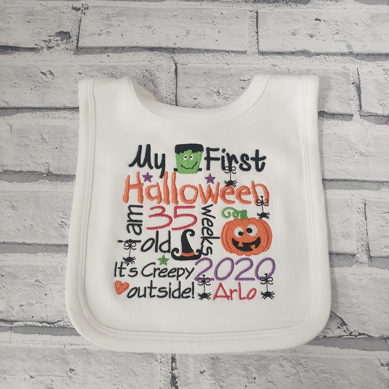 May include: White baby bib with embroidered text that reads "My First Halloween I am 35 weeks old It's Creepy Outside! 2020 Arlo" with a green monster, a witch's hat, a pumpkin, and spiders.