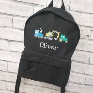 May include: Black backpack with embroidered images of a blue train, yellow excavator, and green tractor. The name "Oliver" is embroidered in white below the vehicles. The backpack has a front pocket and adjustable straps.