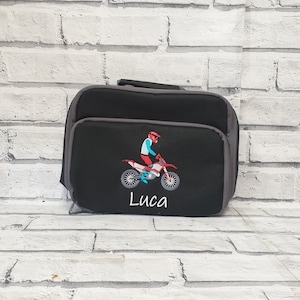 May include: Black lunch bag with a grey trim. The bag features an embroidered design of a person riding a dirt bike and the name "Luca".