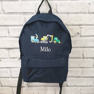 May include: Navy blue backpack with embroidered construction vehicles: a train, excavator, and tractor. The name "Milo" is embroidered below the vehicles. The backpack has a front pocket, black straps, and a top handle.