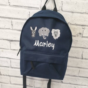 May include: A navy blue backpack with a zipped pocket and adjustable straps. The backpack features an embroidered design of a zebra, elephant, and lion, with the name "Marley" embroidered below the animals.