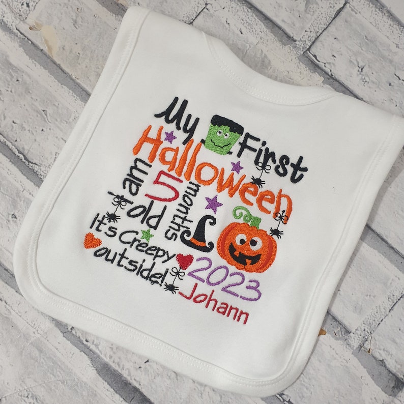 May include: White baby bib with embroidered text that reads "My First Halloween I am 5 months old It's Creepy outside! 2023 Johann" with a pumpkin, witch hat, and Frankenstein monster graphic.