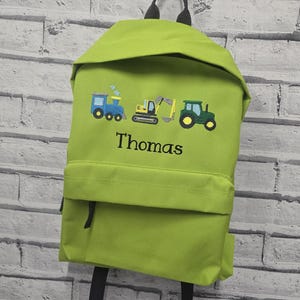 May include: Lime green backpack with embroidered images of a blue train, yellow excavator, and green tractor. The name "Thomas" is embroidered below the images. The backpack has black straps and a front pocket.