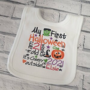 May include: White baby bib with embroidered text that reads "My First Halloween I am 21 weeks old It's Creepy outside! 2021 Elsie" with a pumpkin, witch hat, spider, and monster graphics.