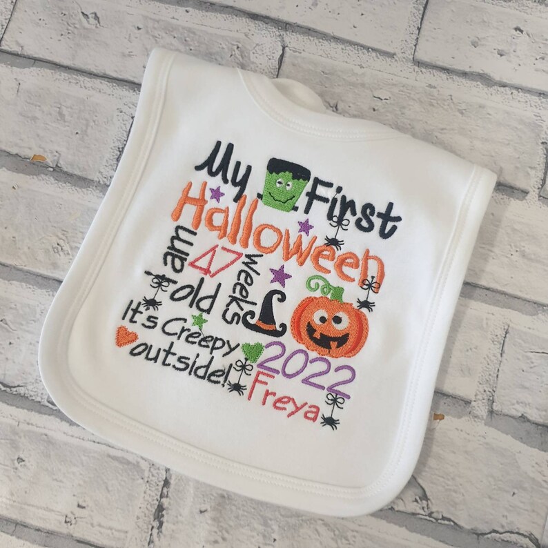 May include: White baby bib with embroidered text that says "My First Halloween I am 47 weeks old It's Creepy outside! 2022 Freya" with a pumpkin, witch hat, and monster graphic.
