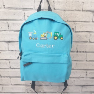 May include: A turquoise backpack with a front pocket and black straps. The backpack features embroidered images of a blue train, a yellow excavator, and a green tractor. The name "Carter" is embroidered in white below the vehicles.