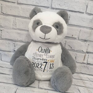 Pu&ograve; includere: Un orso panda di peluche con pelliccia bianca e grigia, caratterizzato da un testo ricamato sul petto che recita Oliver Henry Elmar, Thursday 9th June 2022, 7 Pounds 13 oz, 11:37PM, arricchito da piccole stelle dorate e una corona dorata.