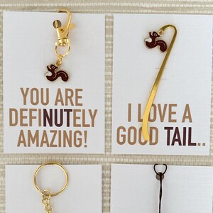 May include: Four cards with accessories. One card has a gold keychain with a brown and gold charm. Another has a gold bookmark with a brown and gold charm. The other two cards have keychains and a phone charm with the same charm. Each card has text that reads "YOU ARE DEFINITELY AMAZING!" or "I LOVE A GOLD TAIL.."