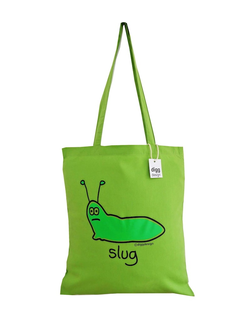 May include: A green tote bag with a cartoon slug illustration and the word "slug" printed on it. The bag has a white tag with the text "digg design" on it.
