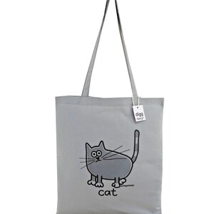 May include: A gray canvas tote bag with a cartoon cat design. The cat is gray with black eyes and a black outline. The bag has a gray handle and the text "digg design" is printed on a white tag attached to the bag. The text "cat" is printed below the cat.