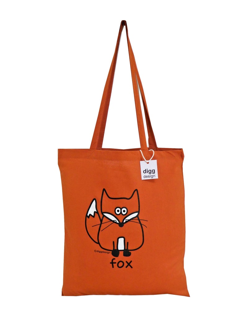 May include: Orange canvas tote bag with a black and white illustration of a fox. The bag has a white tag with the text "digg design" on it. The fox is sitting down with its tail curled behind it. The text "fox" is below the fox.