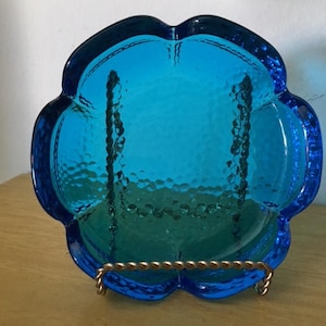May include: A blue glass dish with a hammered texture and a scalloped edge. The dish is on a gold metal stand.