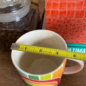Puede incluir: Una taza de caf&eacute; de cer&aacute;mica con un dise&ntilde;o abstracto y colorido. La taza presenta un arco&iacute;ris de colores que incluyen verde, amarillo, naranja y rojo. La taza tiene aproximadamente 10 cm de di&aacute;metro.