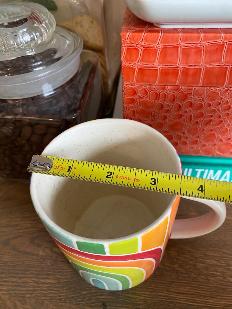 Puede incluir: Una taza de caf&eacute; de cer&aacute;mica con un dise&ntilde;o abstracto y colorido. La taza presenta un arco&iacute;ris de colores que incluyen verde, amarillo, naranja y rojo. La taza tiene aproximadamente 10 cm de di&aacute;metro.