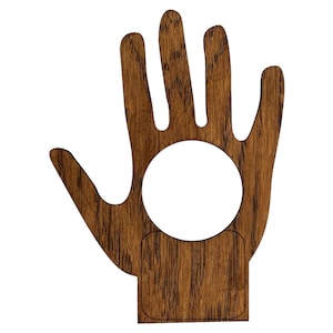 Może przedstawiać: Drewniany ornament w kształcie dłoni z okrągłym wycięciem w dłoni i prostokątnym wycięciem w nadgarstku. Ornament jest zabarwiony na ciemnobrązowy kolor.