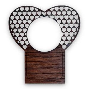 Może przedstawiać: Drewniana ramka w kształcie serca z wyciętym wzorem małych serduszek. Ramka ma prostokątną drewnianą podstawę i okrągły otwór w środku.