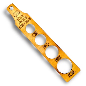 May include: Wooden spaghetti portioner with four graduated circles labelled "one", "two", "three", and "four". The portioner has a handle with a chef's hat and the text "Pasta Spaghetti Portionizer".