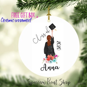 May include: White ceramic ornament with a watercolor illustration of a graduate throwing their cap in the air. The text "Class of 2020" and the name "Anna" are written on the ornament.