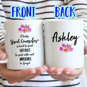 May include: Two white coffee mugs with black text and floral designs. The front mug reads "A truly Great Counselor is hard to find, Difficult to part with and Impossible to forget". The back mug reads "Ashley".