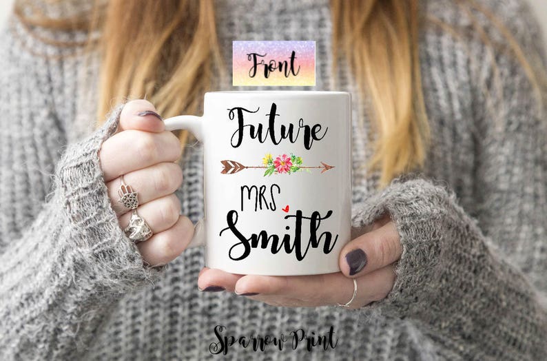 K&ouml;nnte beinhalten: Eine wei&szlig;e Keramiktasse mit einem schwarzen Pfeil und einem Blumenmuster. Der Text "Future Mrs. Smith" ist auf die Tasse gedruckt.