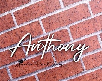 May include: A wooden name sign with the name "Anthony" written in a cursive font. The sign is on a brick wall background.