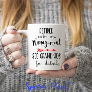 May include: White ceramic coffee mug with black text that reads "Retired under new management see grandkids for details". A red arrow points to the right with a small heart at the end of the arrow.