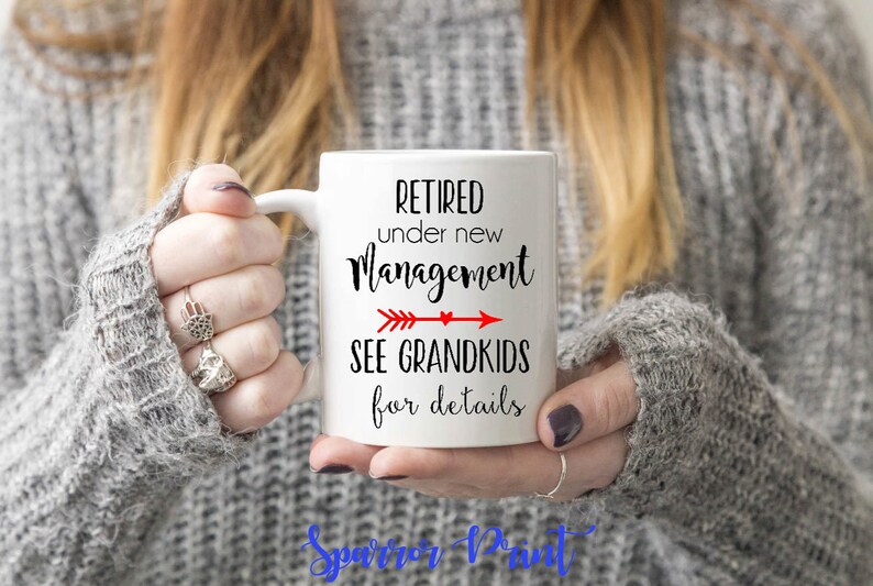 May include: White ceramic coffee mug with black text that reads "Retired under new management see grandkids for details". A red arrow points to the right with a small heart at the end of the arrow.