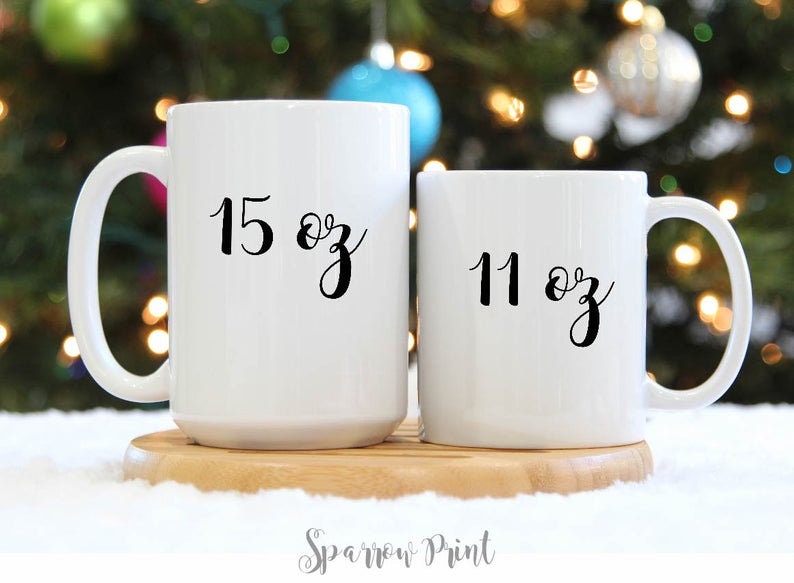 May include: Two white ceramic mugs with black lettering. The larger mug is 15 oz and the smaller mug is 11 oz.