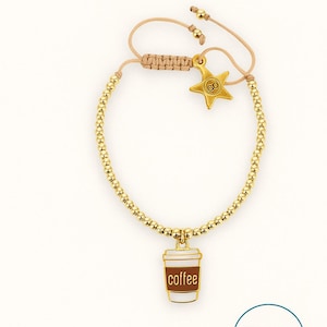 Puede incluir: Pulsera dorada con cuentas con un dije de taza de café y un dije de estrella. El dije de la taza de café tiene la palabra "coffee" impresa. El dije de estrella tiene la palabra "GO" impresa. La pulsera es ajustable.