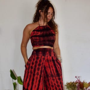 May include: A two-piece tie-dye outfit in red and black. The halter top and wide-leg pants have a vertical stripe pattern. The pants have pockets and are embellished with small, scattered beads. The outfit is paired with platform boots.